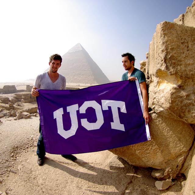 Two male students near pyramid with TCU flag