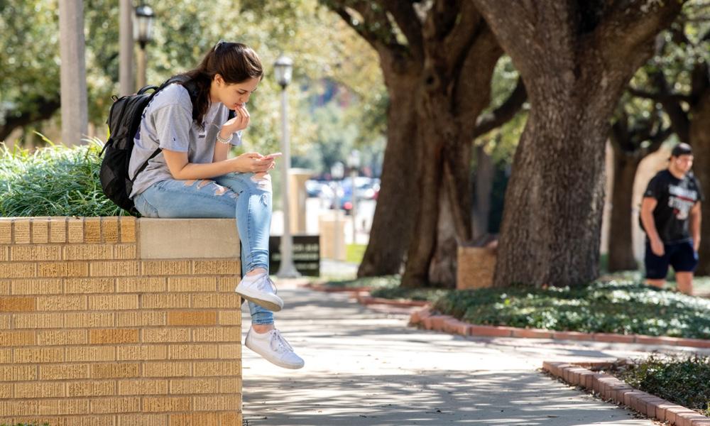 female student on campus sitting on a wall